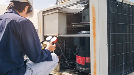 Technician servicing an outdoor air conditioning unit with gauges